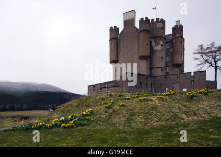 Braemar Castle in Scozia, con narcisi in fiore nella parte anteriore del castello e la neve sulla cima della montagna in background. Foto Stock