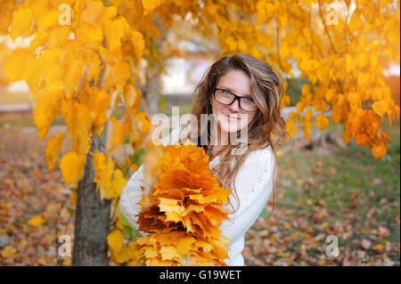 Bellissima ragazza con gli occhiali in giallo le foglie di autunno nel parco Foto Stock