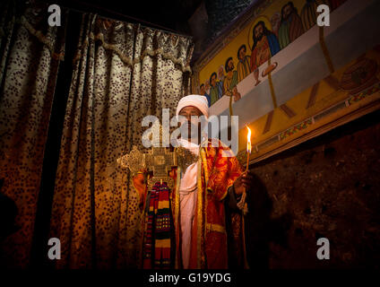 Ortodossa Etiope sacerdote tenendo una croce all'interno di una chiesa rupestre, Amhara Region, Lalibela, Etiopia Foto Stock