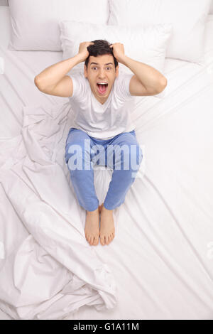 Colpo verticale di un uomo arrabbiato che soffrono di insonnia e urlando seduto su un letto Foto Stock