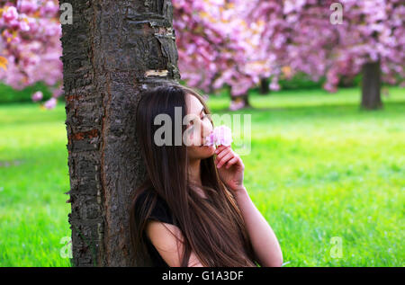 Felice bella giovane donna in fiore parco con alberi e fiori. Foto Stock