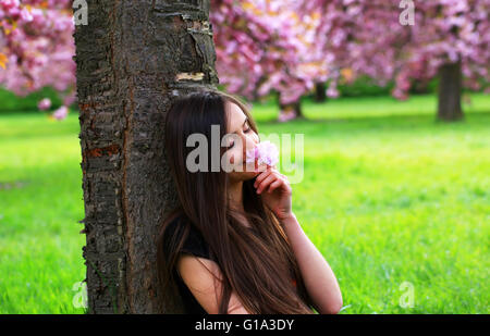 Felice bella giovane donna in fiore parco con alberi e fiori. Foto Stock