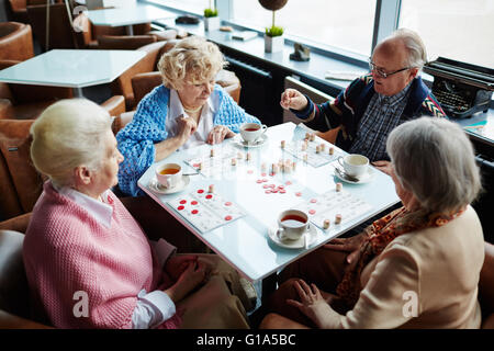 Gruppo di amici senior riproduzione lotto da tavola in cafe Foto Stock