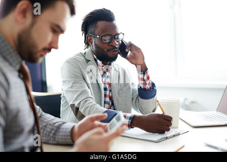 Giovane africano dipendente parlando al telefono con il collega vicino Foto Stock