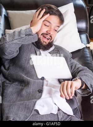 Assonnato imprenditore con un dispositivo tablet pc su un divano Foto Stock
