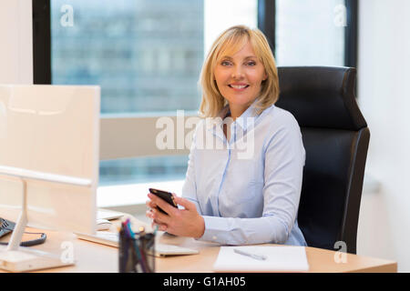 Sorridente di mezza età donna business lavora in un ufficio moderno. Guardando la fotocamera Foto Stock