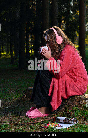 La donna è seduta in accappatoio nella foresta e bere da una m Foto Stock