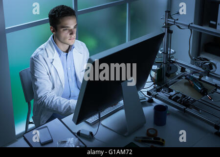 Fiducioso studente di ingegneria lavorando nel laboratorio e utilizzando un computer, stampante 3D in background, tecnologia e innov Foto Stock