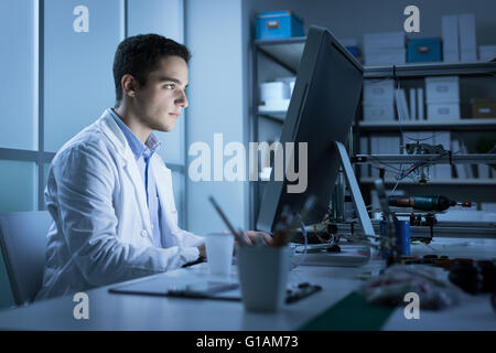 Fiducioso studente di ingegneria lavorando nel laboratorio e utilizzando un computer, stampante 3D in background, tecnologia e innov Foto Stock