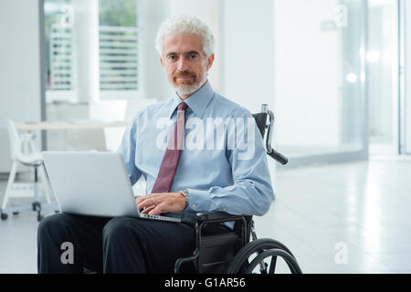 Successo imprenditore aziendale in sedia a rotelle in ufficio utilizzando un computer portatile e funzionante Foto Stock