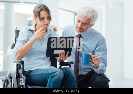 Imprenditore che mostra un documento su un appunti per una giovane donna in sedia a rotelle, assistenza e aiuto concetto Foto Stock