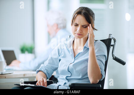 Disabili business donna in carrozzella a ufficio avente un mal di testa di toccare i suoi templi Foto Stock