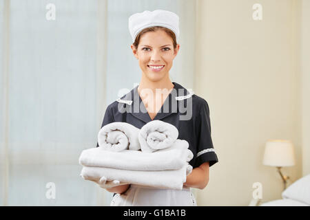 Maid in uniforme durante il servizio di pulizie in una camera di hotel azienda freschi asciugamani puliti Foto Stock