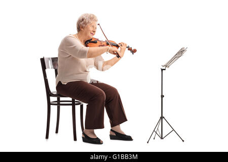 Femmina matura il violinista riproduzione di un violino seduto su una sedia in legno isolato su sfondo bianco Foto Stock