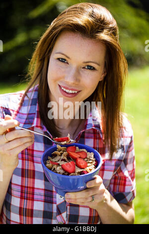 Ritratto di una donna al di fuori del mangiare sano cereali per la prima colazione con fragole fresche frutta Foto Stock