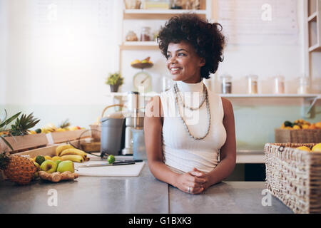 Ritratto di giovane e bella donna che lavorano al bar dei succhi, ella è in piedi dietro il contatore che guarda lontano e sorridente. Foto Stock