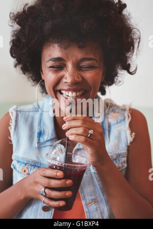 Close up ritratto di allegro giovane donna di bere succo di frutta fresco e sorridente. Felice giovane africano modello femminile avente un drin Foto Stock