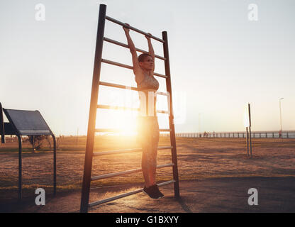 A piena lunghezza shot di montare la giovane donna in abbigliamento sportivo esercita sulla parete bar all'aperto durante il tramonto. Donna Fitness facendo stretching Foto Stock