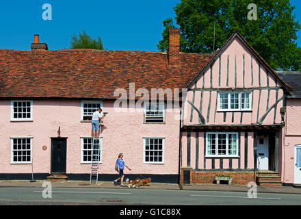 Uomo sulla scaletta, riparazione dei telai di finestra sulla casa del villaggio di Lavenham, Suffolk, Inghilterra, Regno Unito Foto Stock