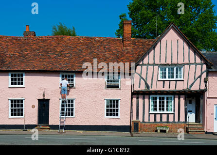 Uomo sulla scaletta, riparazione dei telai di finestra sulla casa del villaggio di Lavenham, Suffolk, Inghilterra, Regno Unito Foto Stock