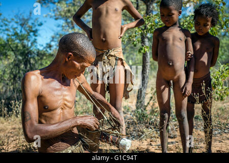 San bambini attorno seduti hunter nel Museo vivente del Ju'Hoansi-San, Grashoek, Namibia Foto Stock