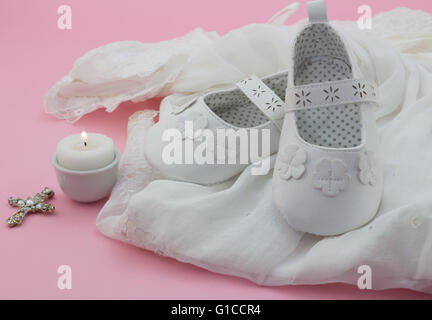 Bambina scarpe, croce e candela sul pizzo bianco con sfondo rosa Foto Stock