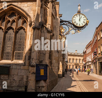 Una vista della trafficata Coney Street nel centro di York con gli ornati hanging orologio da parete su St Martins chiesa Foto Stock