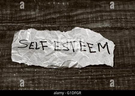 Il testo autostima scritto in un pezzo di carta, posta su un rustico di una superficie di legno, in bianco e nero Foto Stock