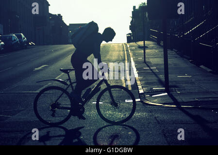 Silhouette di un giovane uomo in bicicletta sulle strade di Glasgow con road contre-jour retroilluminato in Glasgow, Scotland, Regno Unito. Foto Stock