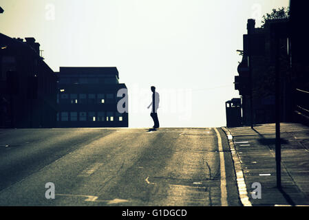 Silhouette di un giovane uomo sulla strada di Glasgow con road contre-jour retroilluminato in Glasgow, Scotland, Regno Unito. Foto Stock