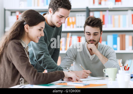 Gruppo di sorridere gli studenti universitari che studiano insieme alla libreria e lavorare a un progetto Foto Stock