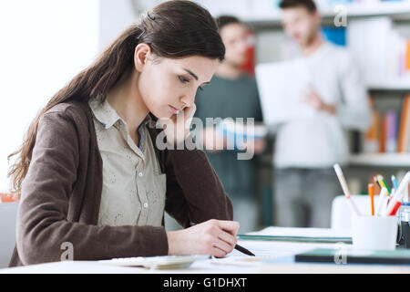 Giovane studentessa di fare i compiti e studiare in biblioteca, gli studenti e gli scaffali su sfondo, l educazione e l apprendimento Foto Stock