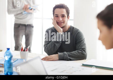 I ragazzi che studiano insieme alla scrivania, uno studente sorride alla telecamera e tenendo una matita, egli sta lavorando su un progetto scolastico Foto Stock