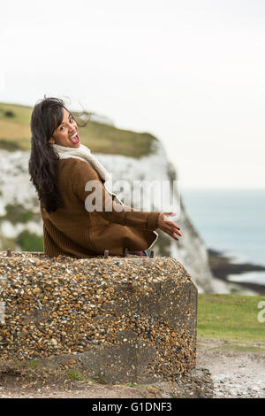 Giovane donna facendo quirky espressione mentre è seduto su una roccia. Le Bianche Scogliere di Dover, Dover, Kent, Regno Unito Foto Stock