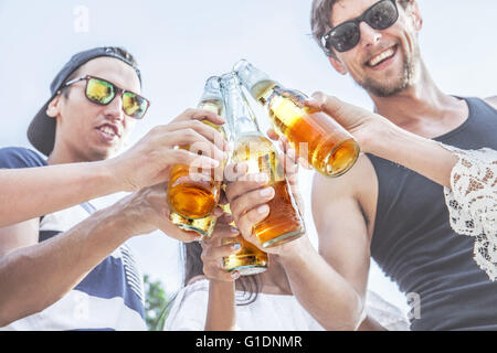 Sorridenti amici tintinnio di bottiglie di birra all'aperto Foto Stock