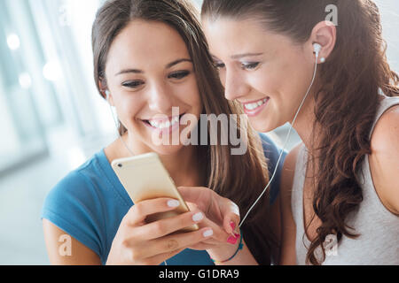 Piuttosto sorridente giovani ragazze la condivisione e gli auricolari per ascoltare la musica usando una smart phone Foto Stock