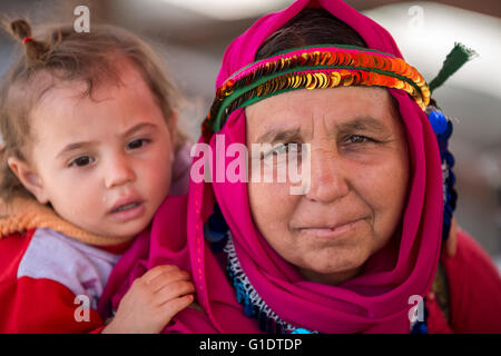 La madre che indossa abiti locali porta il suo bambino sulla sua schiena nella campagna della provincia di Aydin, Turchia. Foto Stock