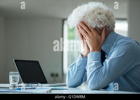 Esaurito imprenditore con testa in mani seduto alla scrivania in ufficio, guasto e concetto di depressione Foto Stock