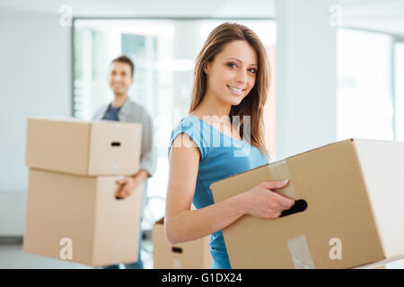 Sorridenti giovane che si muove in una nuova casa e il trasporto di scatole di cartone, delocalizzazioni e concetto di rinnovamento Foto Stock