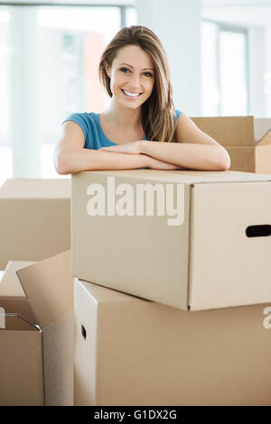 Sorridente giovane donna in movimento nella sua nuova casa e appoggiate su una scatola di cartone Foto Stock