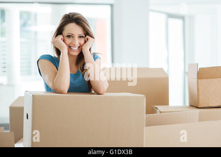 Sorridente giovane donna in movimento nella sua nuova casa e appoggiate su una scatola di cartone Foto Stock