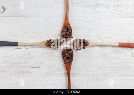 Quattro cucchiai di legno con chicchi di caffè tostati su bianco legno rustico. Vista da sopra con lo spazio di copia Foto Stock