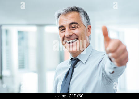 Imprenditore allegro Thumbs up in posa e sorridente in telecamera Foto Stock
