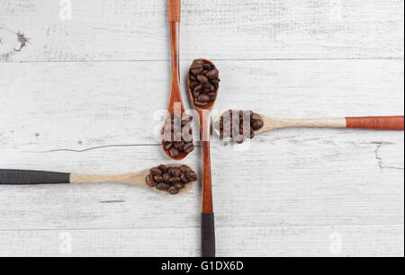 Quattro cucchiai di legno con chicchi di caffè tostati disposti in modo creativo su bianco legno rustico. Vista da sopra con lo spazio di copia Foto Stock