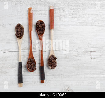 Quattro cucchiai di legno con chicchi di caffè tostati disposti in modo creativo su bianco legno rustico. Vista da sopra con lo spazio di copia Foto Stock