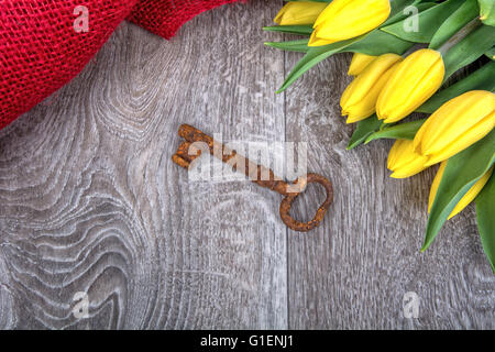 Rusty chiave e tulipano giallo su uno sfondo di legno Foto Stock