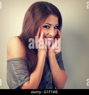 Felice divertente brunette donna tenendo le mani al viso e sogghignando. Tonico ritratto vintage Foto Stock