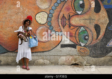 Il sigaro-fumatori donna e il suo gatto di fronte strada murale, Havana, Cuba Foto Stock