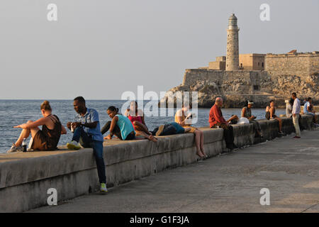 Habaneros rilassarsi sul Malecon parete sul mare nei pressi di Castillo de San Salvador de la Punta, Havana, Cuba Foto Stock