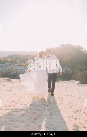 Bello lo sposo in camicia bianca e la sposa indossa l'abito da sposa a piedi kissing sullo sfondo della città Foto Stock